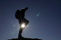 Image of adventure in the uplands - a person stands on top of a hill with the sun shining